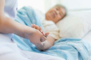 Nurse sitting on a hospital bed next to an older woman helping hands, care for the elderly concept